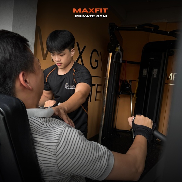 A close-up shot showing a professional trainer supervising a client on weight-lifting equipment within a private gym setting.